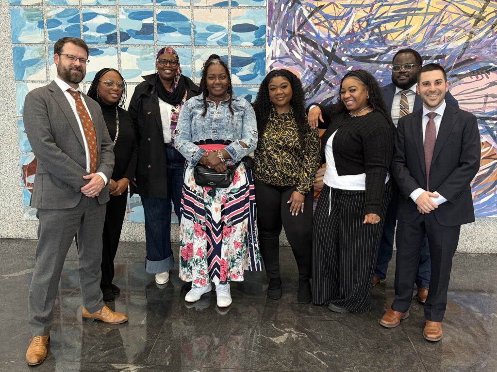 A group of smiling individuals stand in front of two colorful paintings.